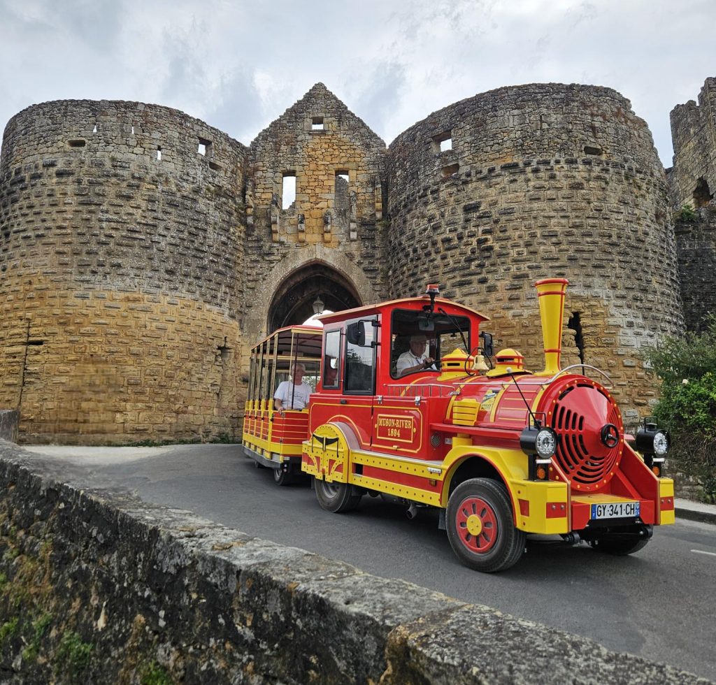 le petit train rouge Domme express passe devant la porte des tours à Domme